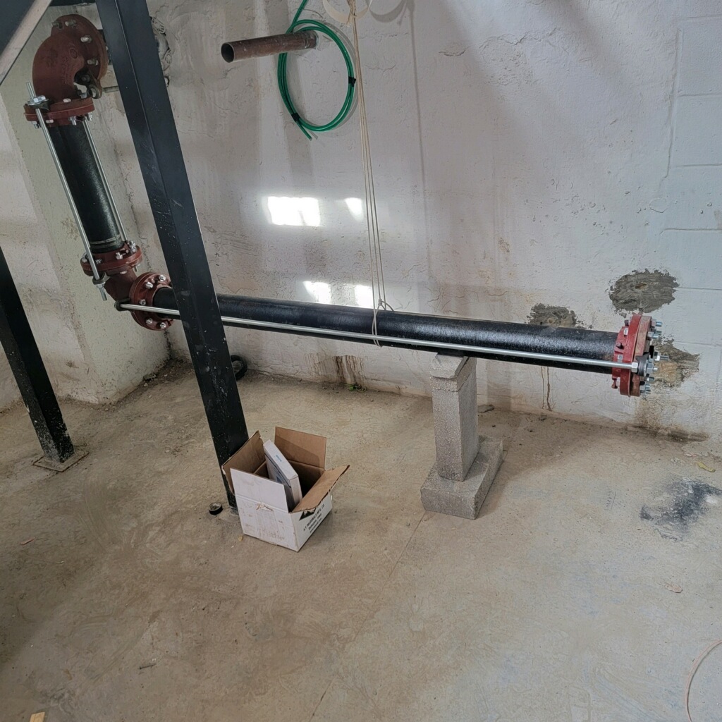 A water main pipe with flanged fittings installed against a foundation wall