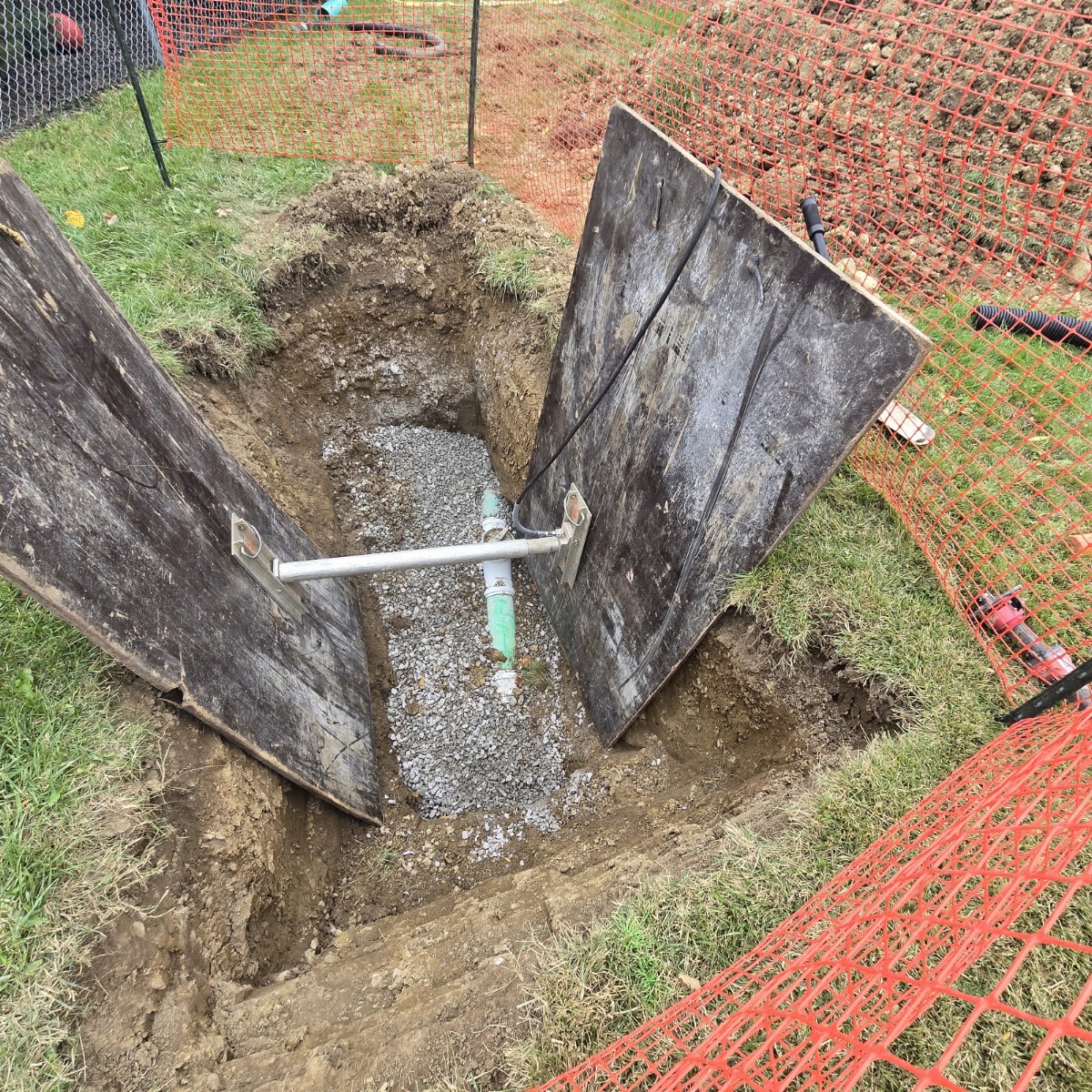 An excavated trench with wooden trench-box shoring and a new pipe connection
